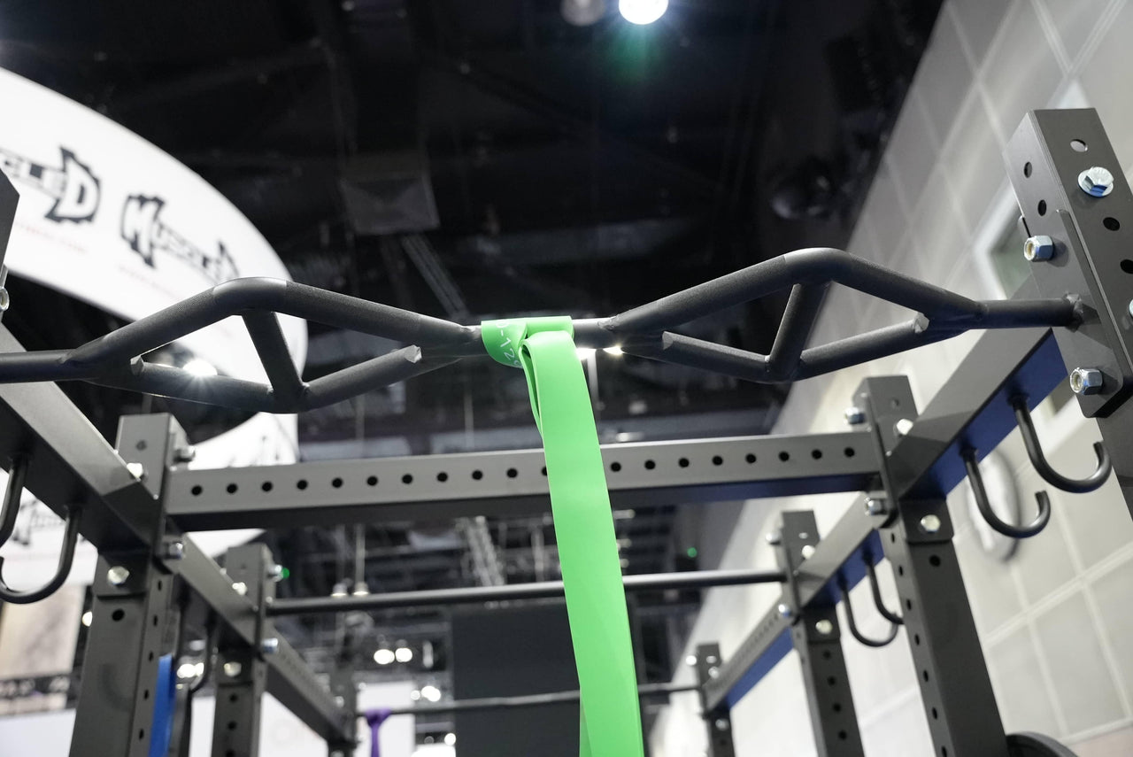 Close-up of a black multi-grip pull-up bar on a squat stand, with a green resistance band attached.