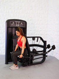 Thumbnail for Woman in red top using a black selectorized triceps press machine in a gym.