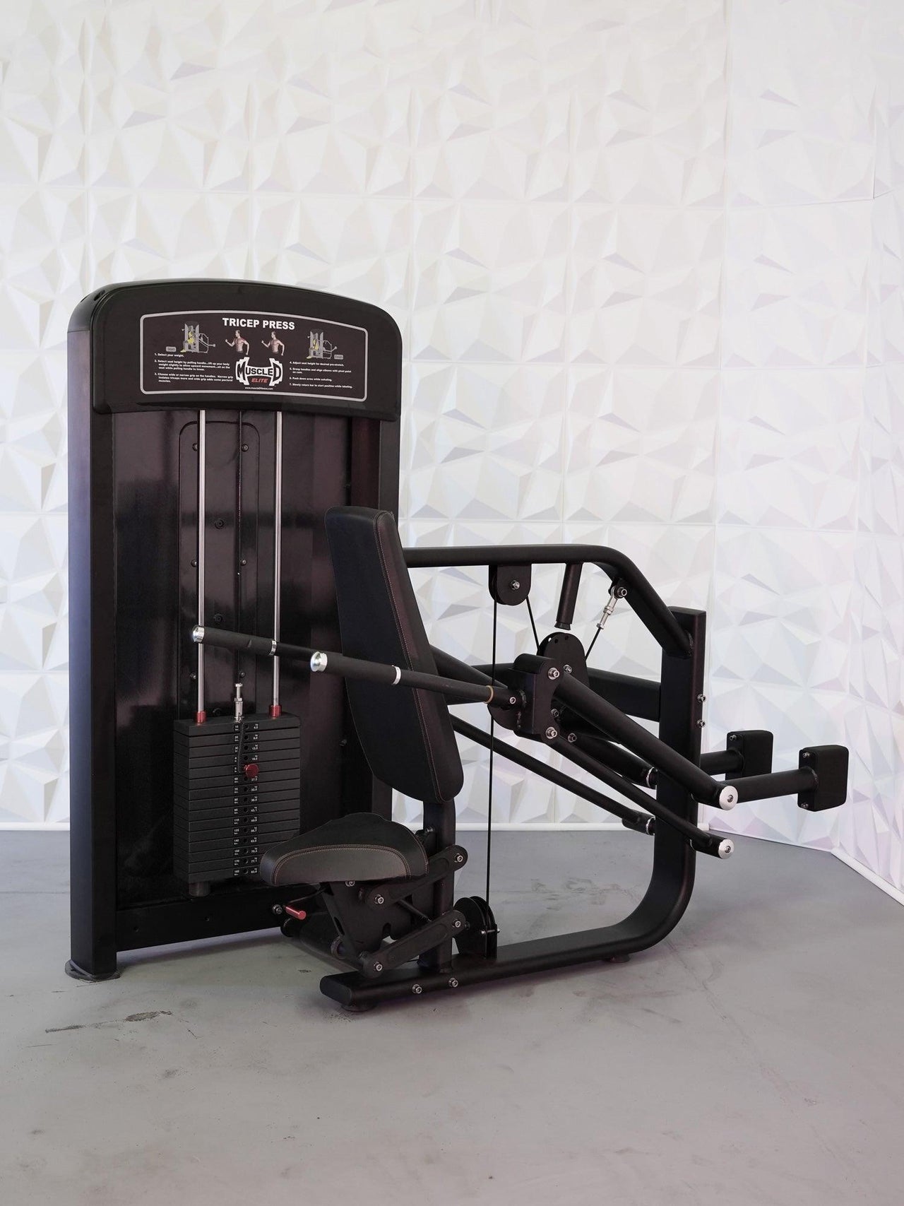 Black commercial triceps press machine with weight stack, padded seat, and arm levers.