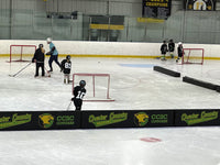 Thumbnail for Black foam rink dividers printed with green Chester County Skating Club and CCSC Cougars logos on an ice rink