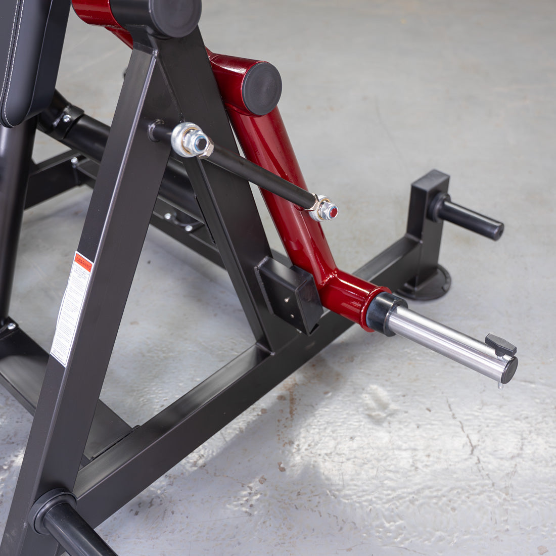 Close-up of a red and black fitness machine's base with a silver weight plate sleeve.