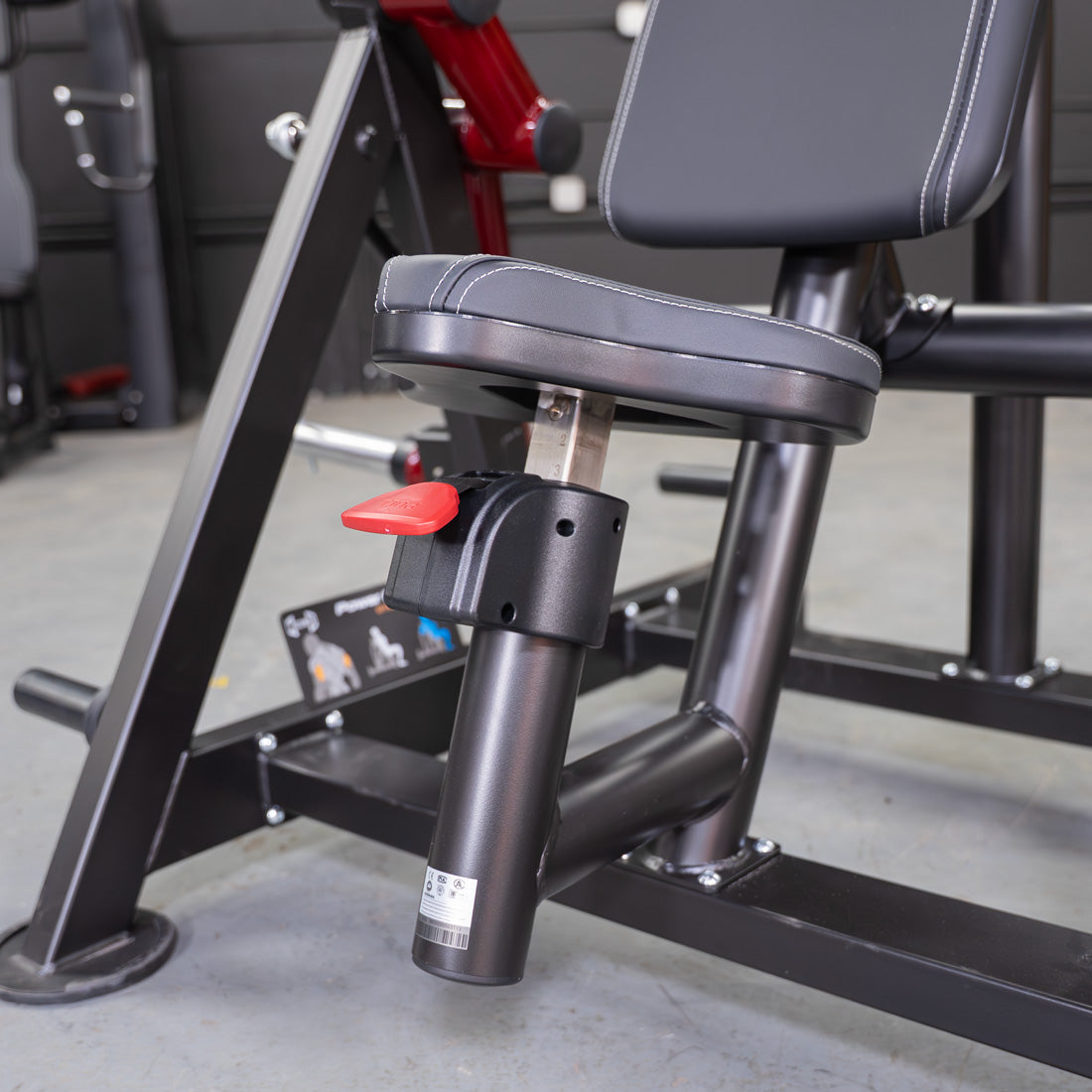 Close-up of a black fitness machine seat with white stitching and a red adjustment lever.