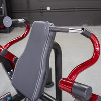 Thumbnail for Close-up of a triceps extension machine with a black padded seat and red curved handles.