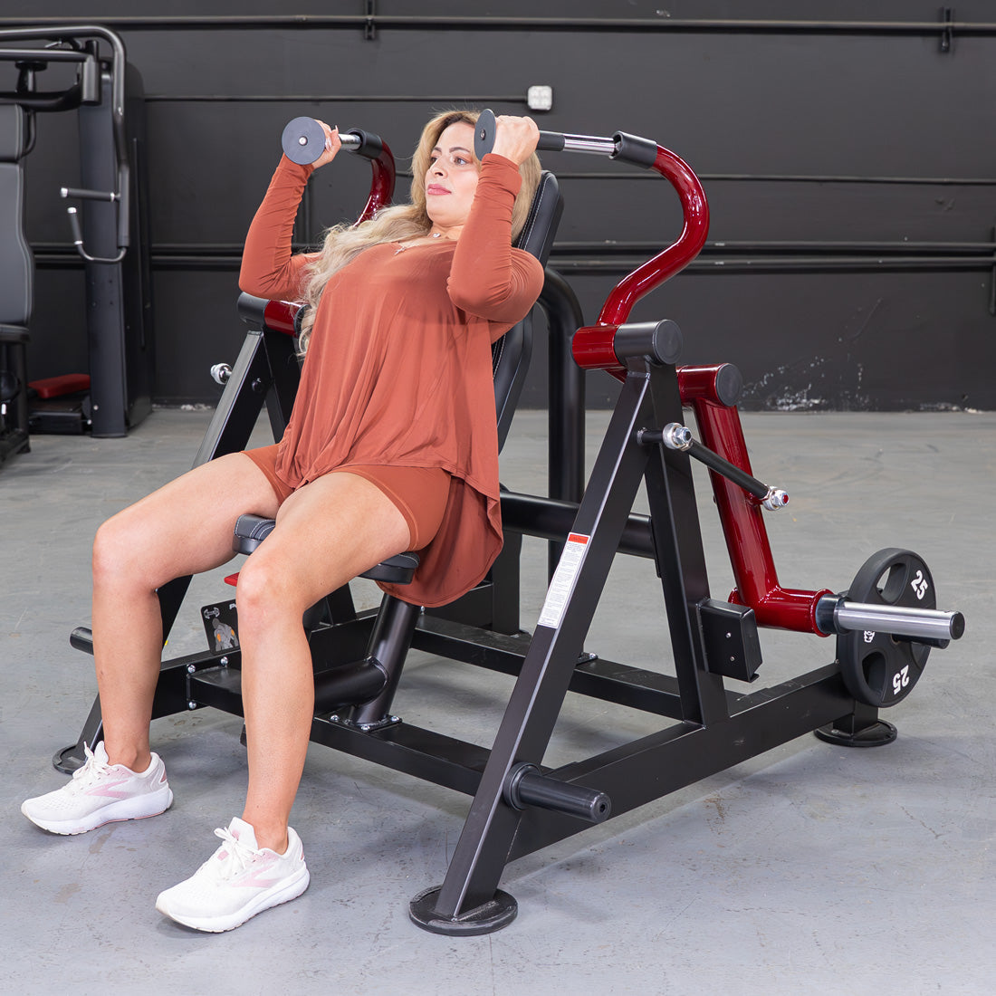 Woman using a red and black triceps extension machine with weight plates in a gym.
