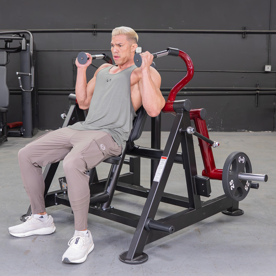 Man in a gym using a red and black triceps extension machine with a 25lb weight plate.