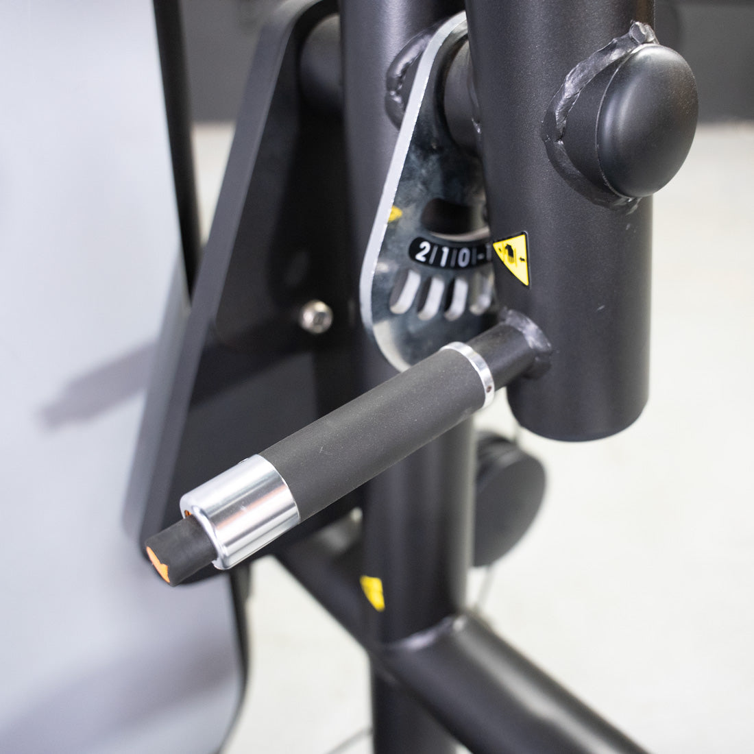 Close-up of a black fitness machine's adjustment pin, showing numbers 2, 1, 0, and a yellow warning symbol.