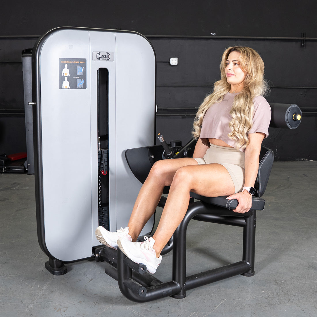 Woman using a gray and black Muscle D Fitness Ab/Back Combo machine in a gym.