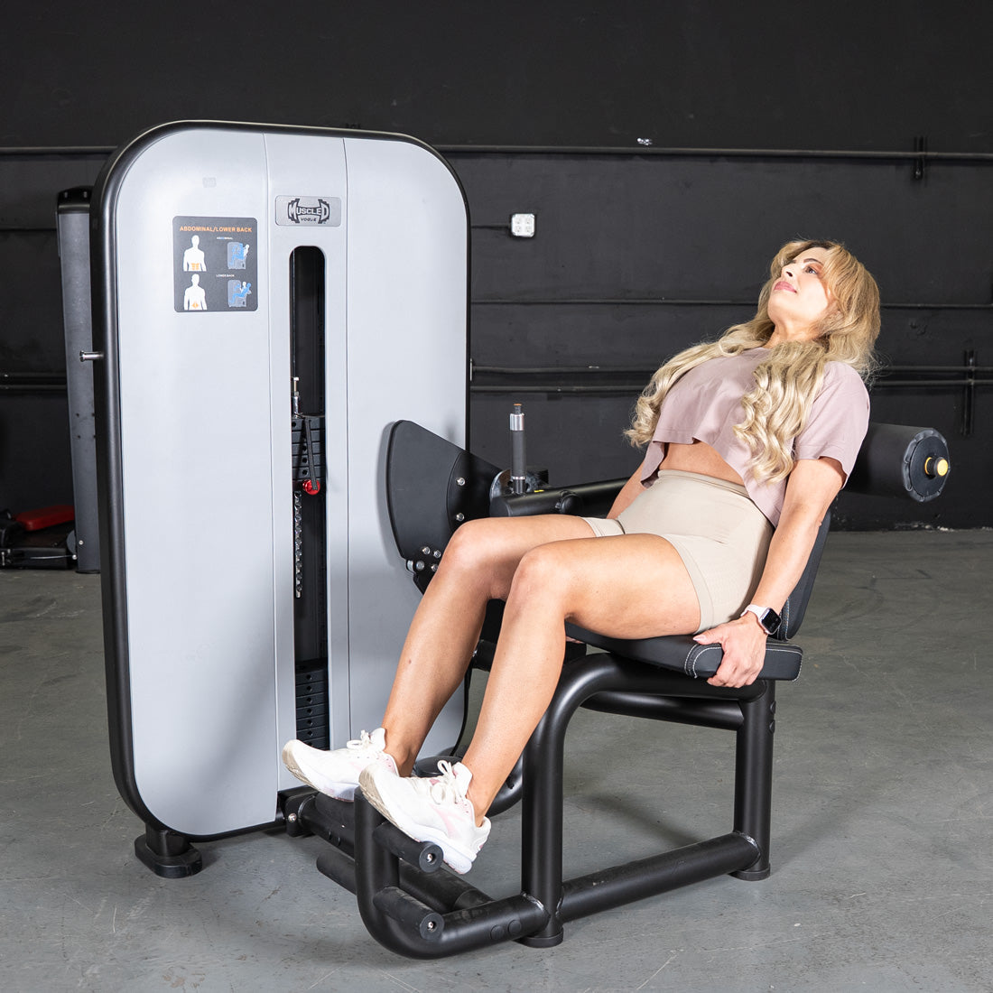 Woman using a gray and black ab/back combo fitness machine in a gym.