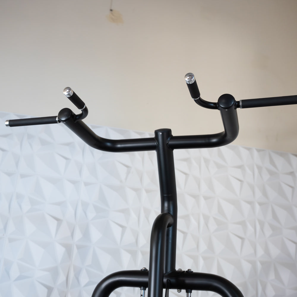 Close-up of the black metal handles of a chin/dip assist machine, with textured white wall in background.