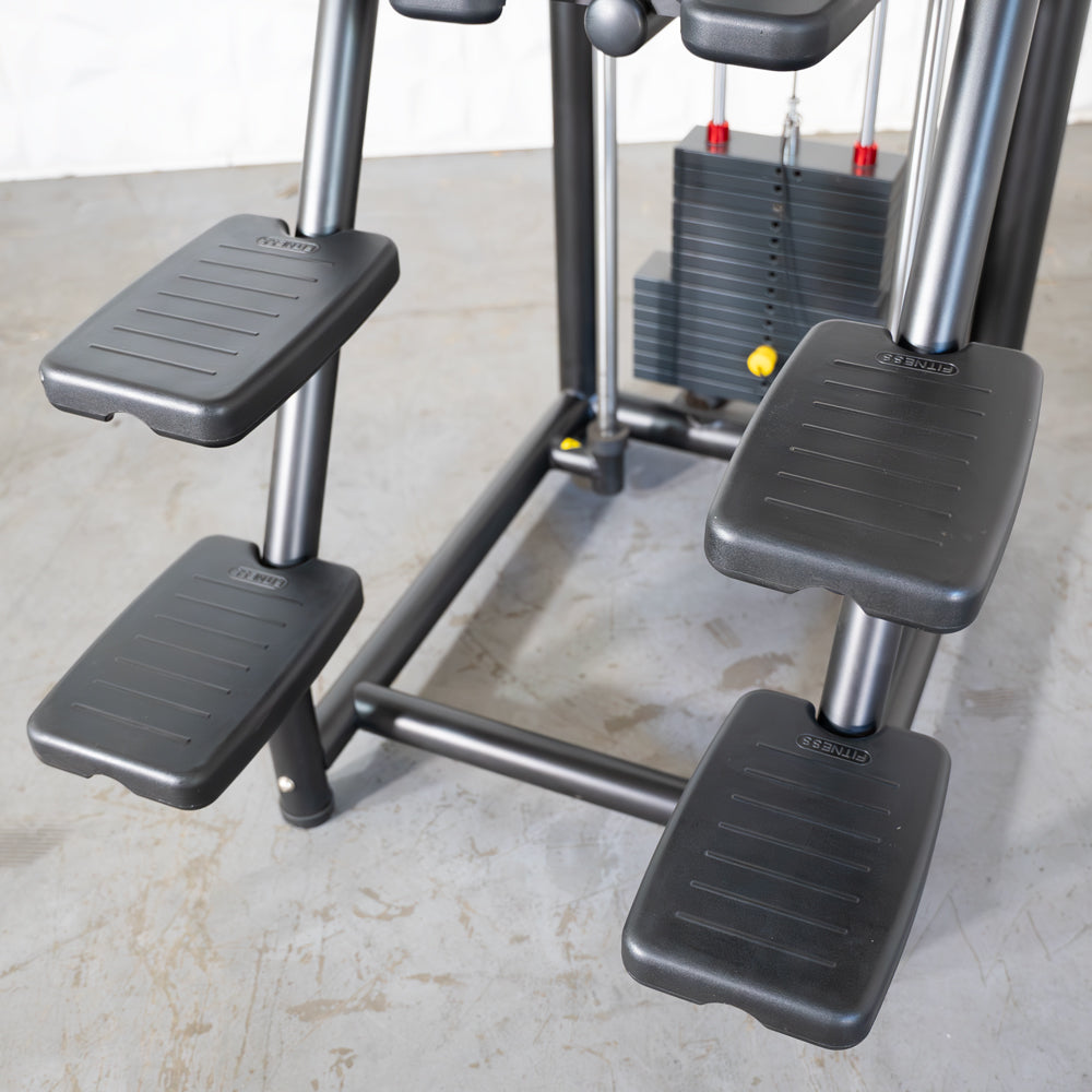 Close-up of the foot platforms and weight stack of an assisted chin/dip machine.