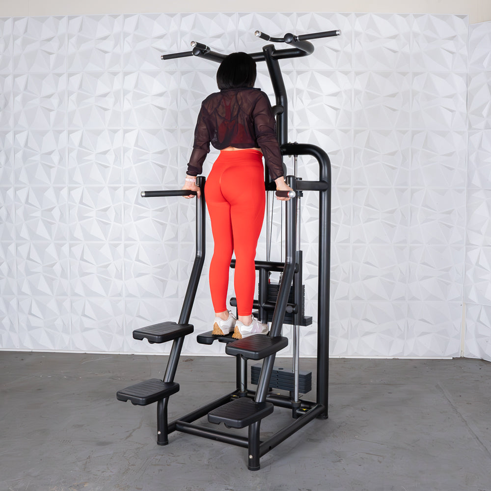 Woman in red leggings using a black assisted chin/dip machine with multiple foot platforms.
