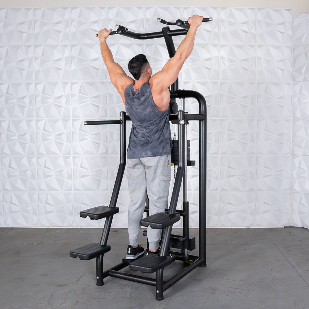 Man using a black assisted chin/dip machine with multiple foot platforms and an overhead bar.