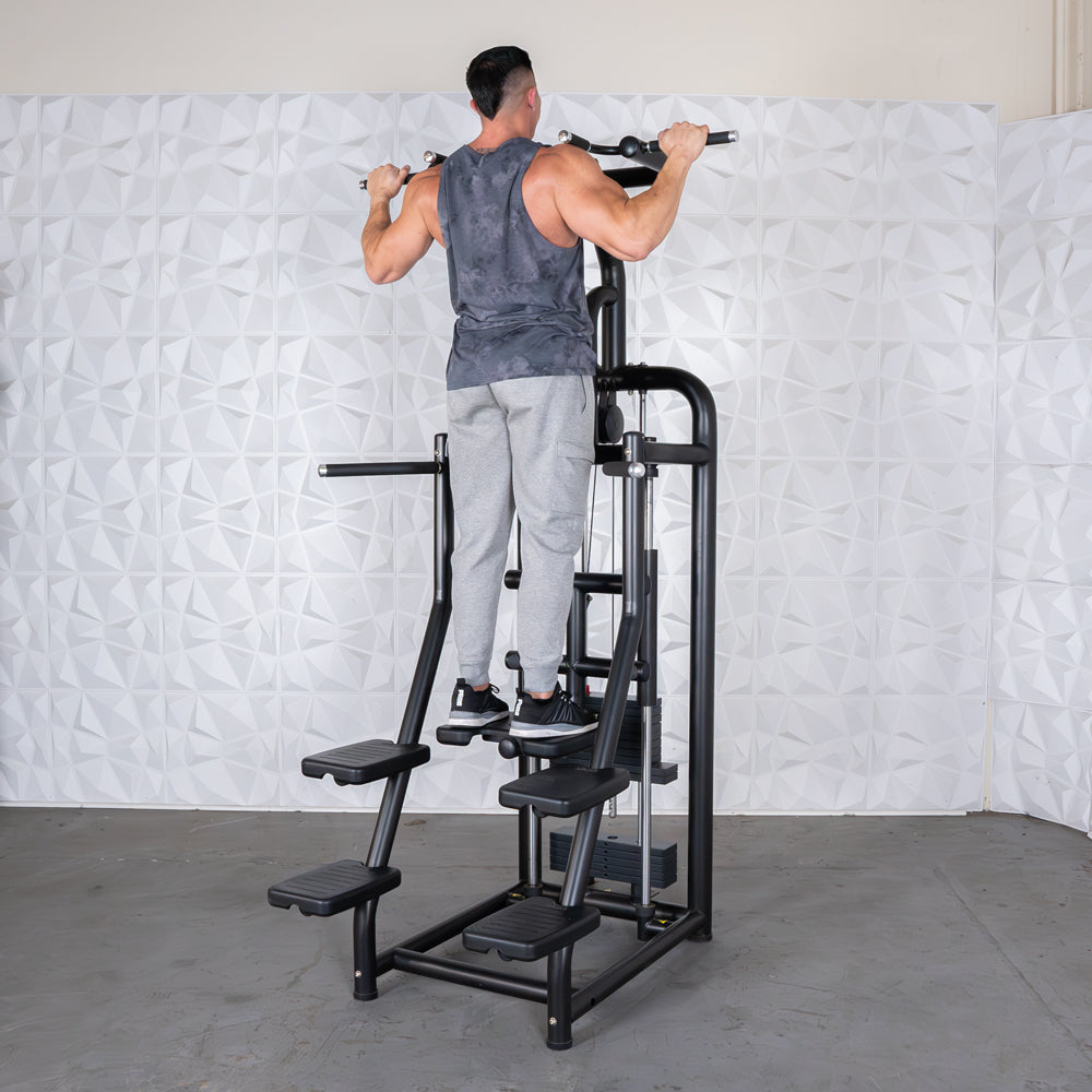 Man performing pull-ups on a black assisted chin/dip machine with white textured wall in background.