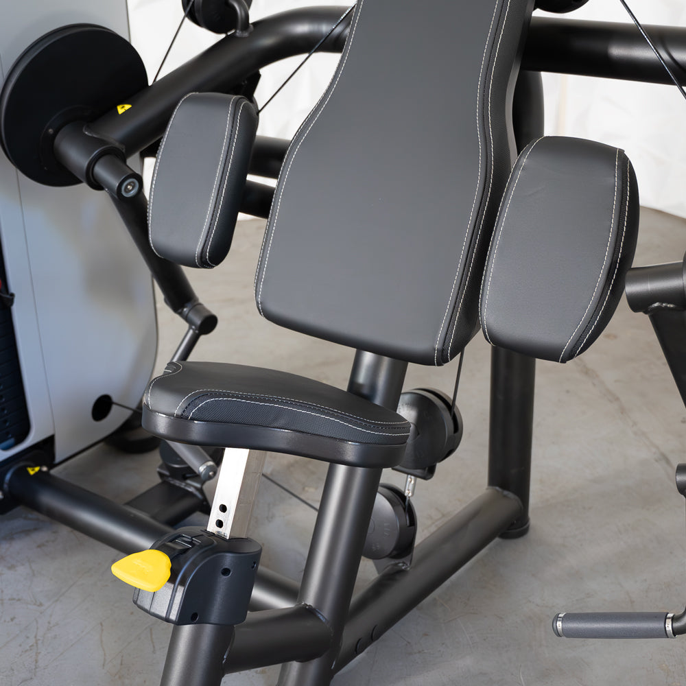 Close-up of a black arm curl machine with padded seat, backrest, and arm pads, featuring white stitching.