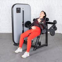 Thumbnail for Woman in red leggings using a black and gray arm curl machine, looking up with a slight smile.