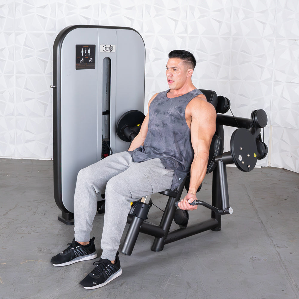 Man in gray tank top and sweatpants using a black and gray arm curl machine.