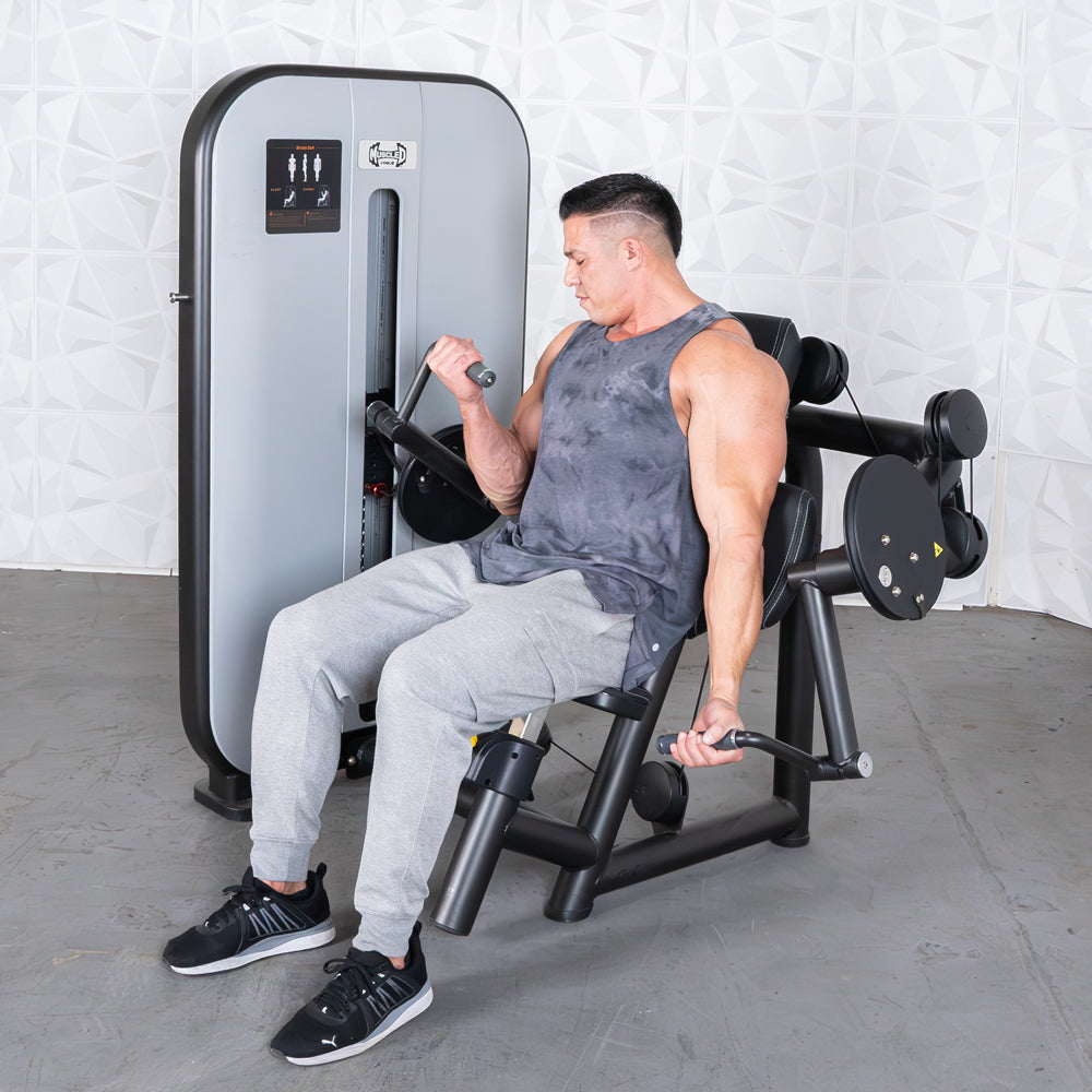 Man in a gray tank top and sweatpants using a black and gray arm curl machine.