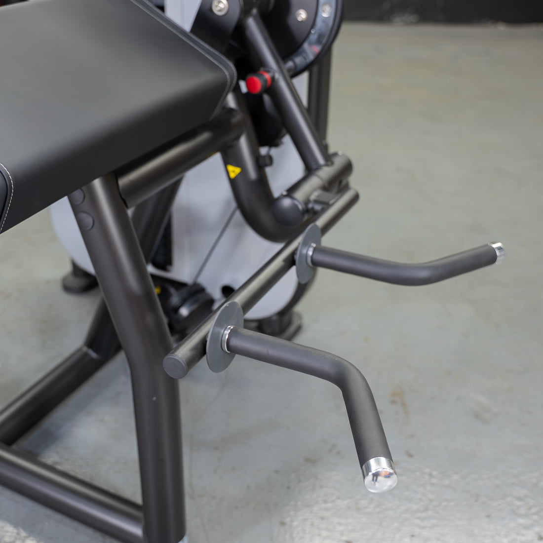 Close-up of a biceps curl machine with a black padded armrest and two curved gray handles.