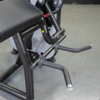Thumbnail for Close-up of a biceps curl machine with a black padded armrest and two curved gray handles.