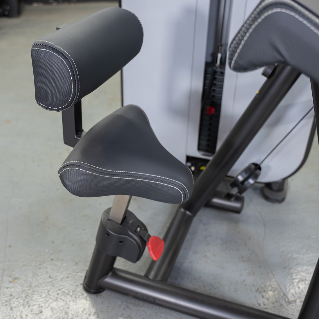Close-up of a black padded seat and armrest on a gym machine, with white stitching.