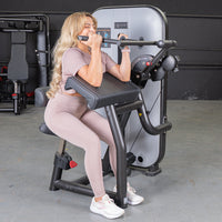 Thumbnail for Woman with long blonde hair using a black and gray biceps curl machine in a gym.
