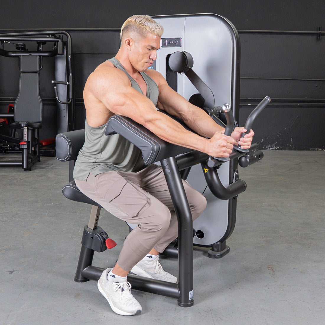 Man with blonde hair using a biceps/triceps combo machine in a gym.