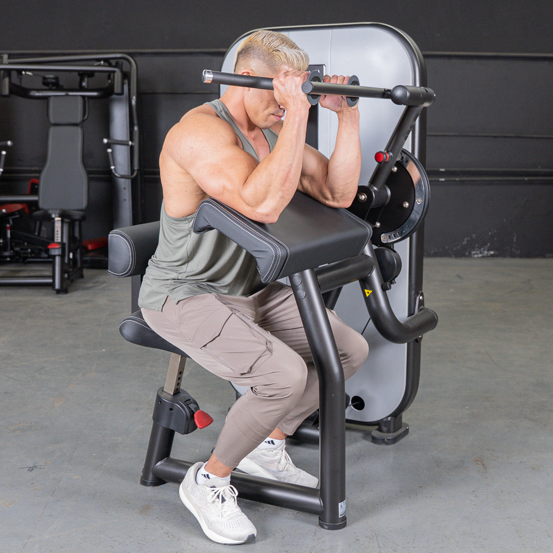 Man using a bicep curl machine in a gym.
