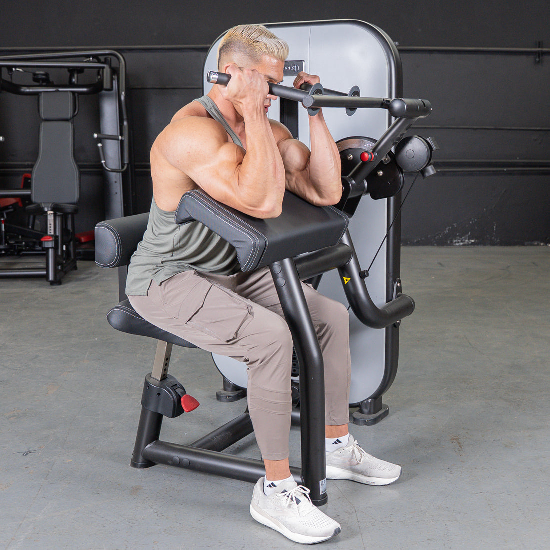 Man using a biceps curl machine in a gym.