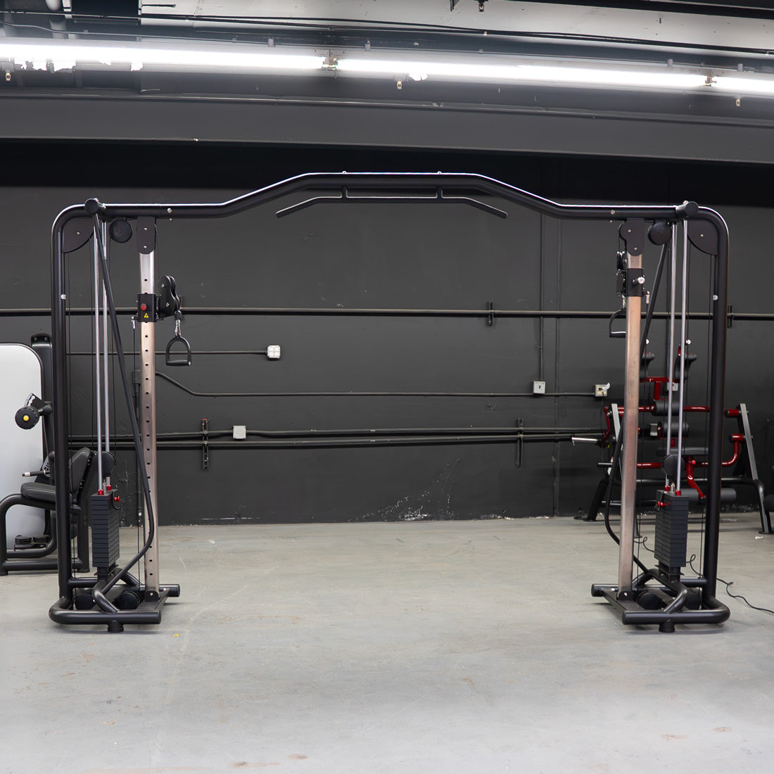 Black cable crossover machine with adjustable pulleys and weight stacks in a gym.
