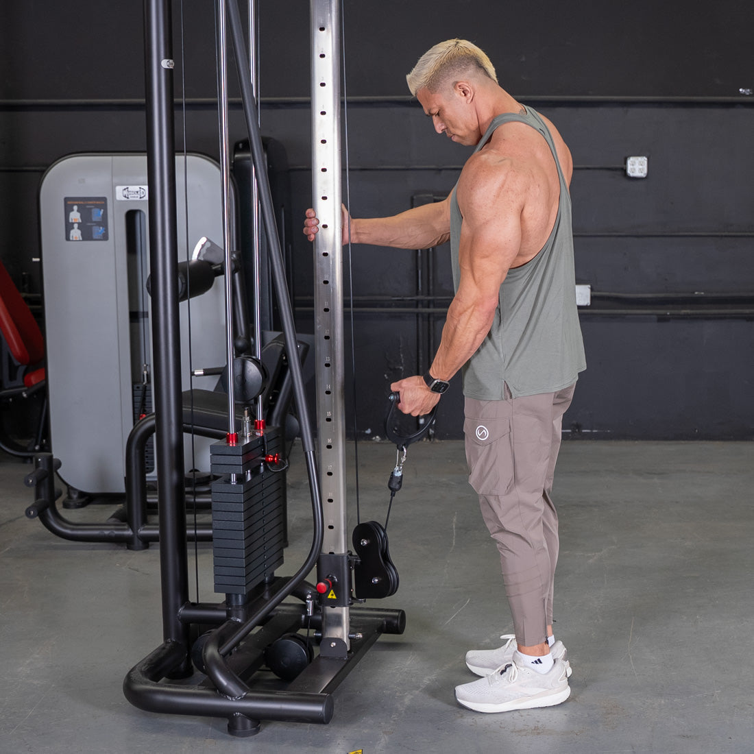 Muscular man using a cable crossover machine for a triceps workout in a gym.