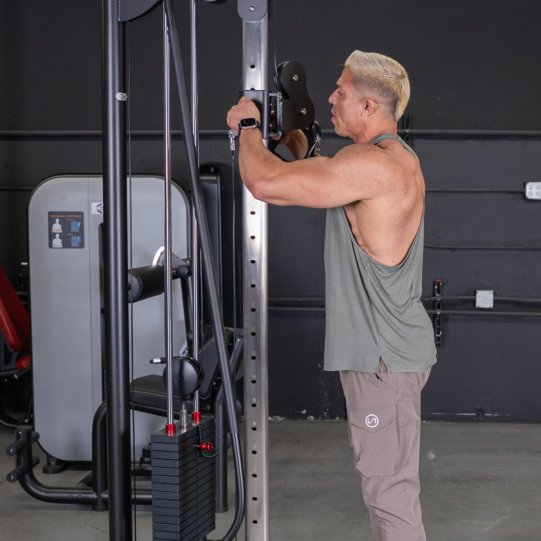 Man adjusting the pulley height on a cable crossover machine in a gym.