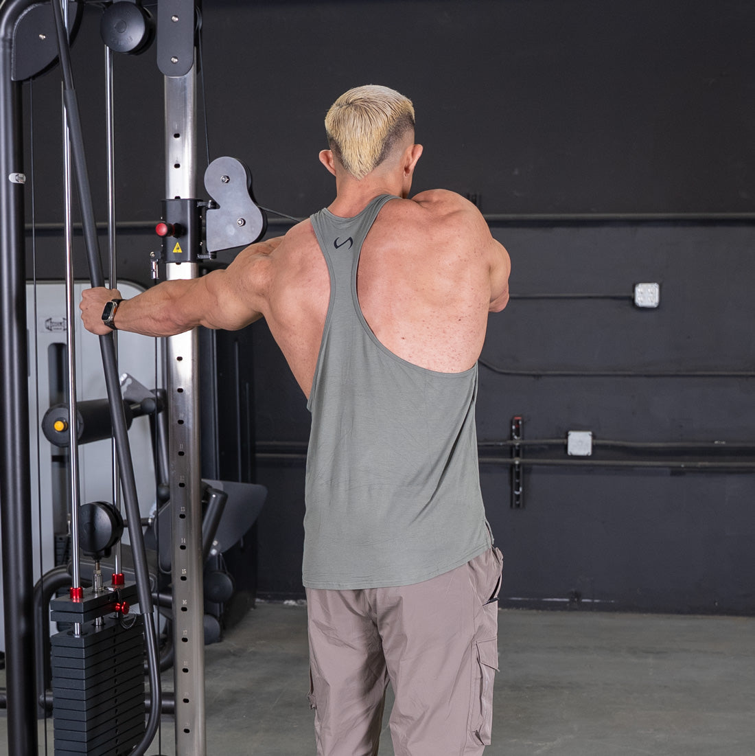 Man in a tank top using a cable crossover machine for a chest or back workout.