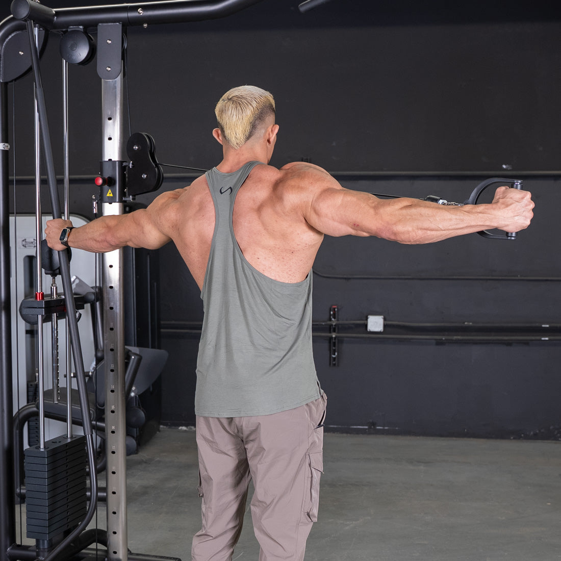 Muscular man in a tank top using a cable crossover machine for a chest workout.