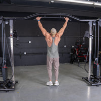 Thumbnail for Man in a tank top doing a wide-grip pull-up on a cable crossover machine in a gym.