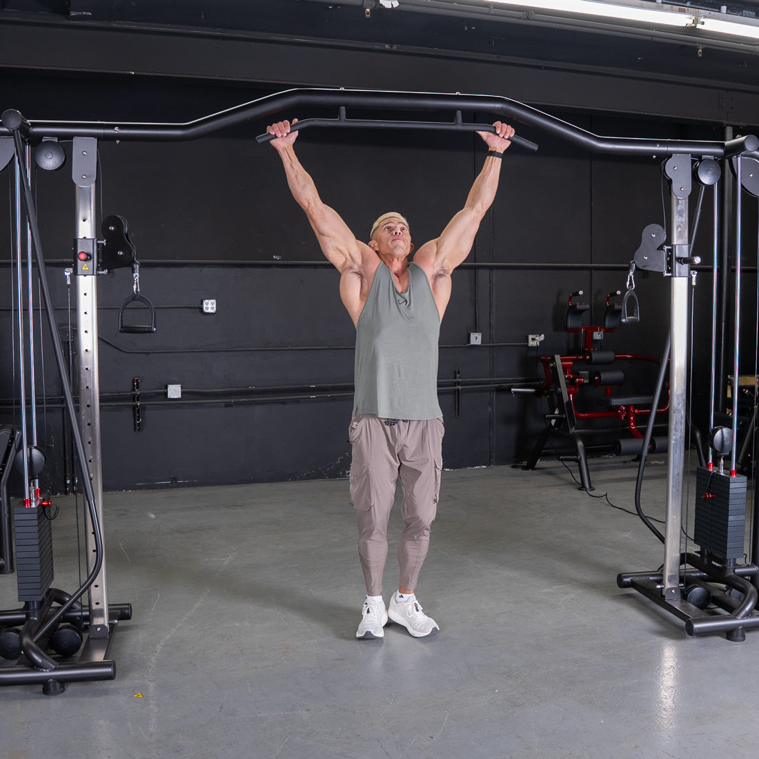 Muscular man in a gym using a cable crossover machine with a pull-up bar attachment.