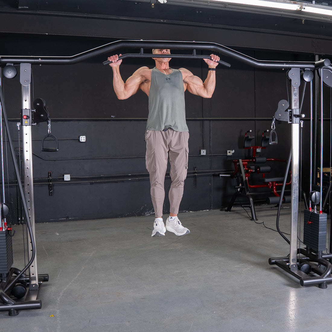 Man doing pull-ups on a cable crossover machine with weight stacks and pull-up bar.