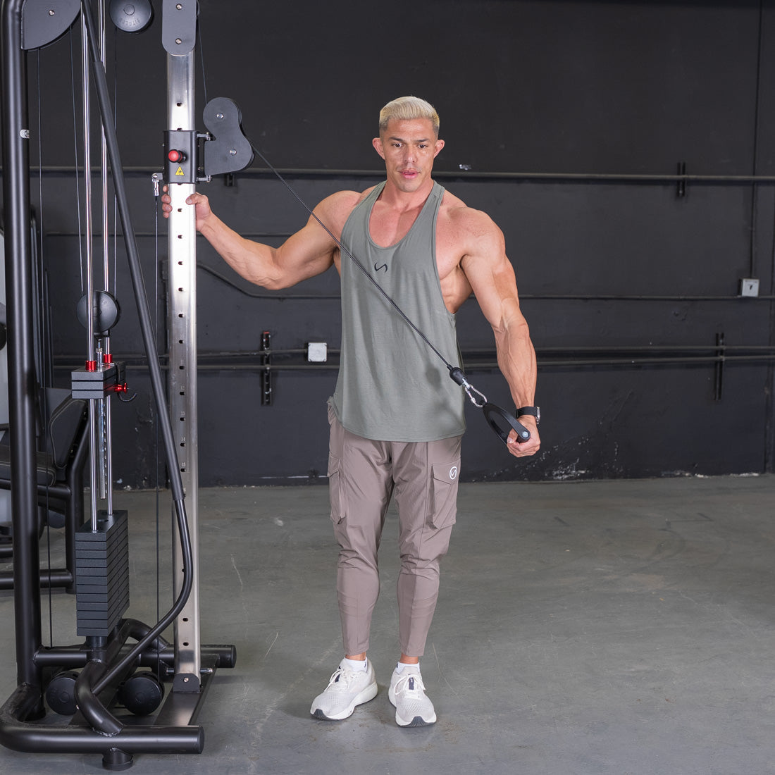 Man in tank top and cargo pants using a cable crossover machine.