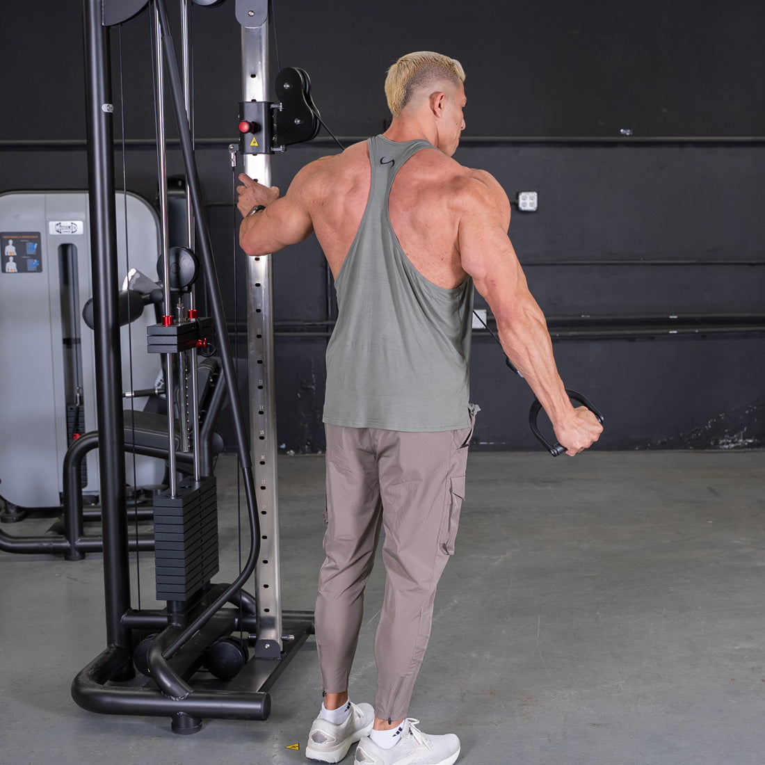 Muscular man in a tank top using a cable crossover machine for a chest or back workout.