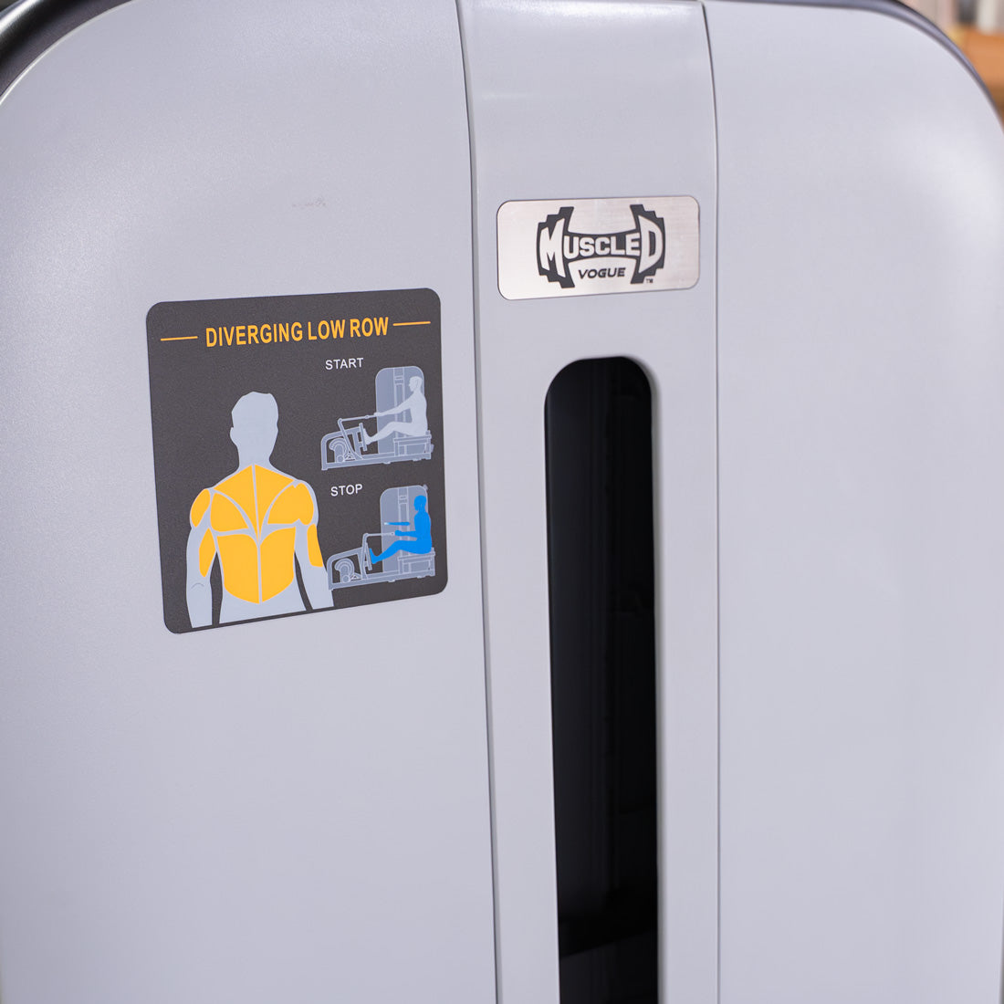 Close-up of a "Diverging Low Row" exercise diagram on a grey "Muscle Vogue" gym machine.