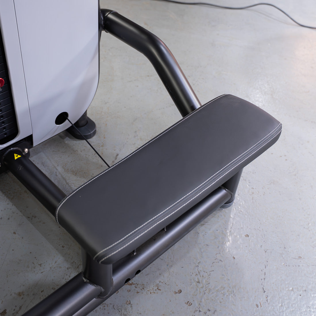 Close-up of a black padded seat with white stitching on a low row gym machine.