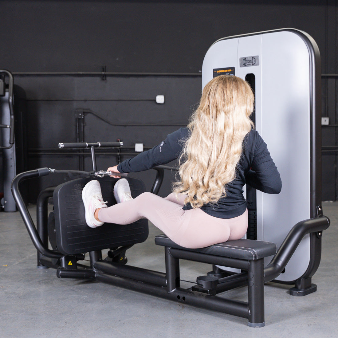Woman using a seated low row machine with a pin selectorized weight stack.
