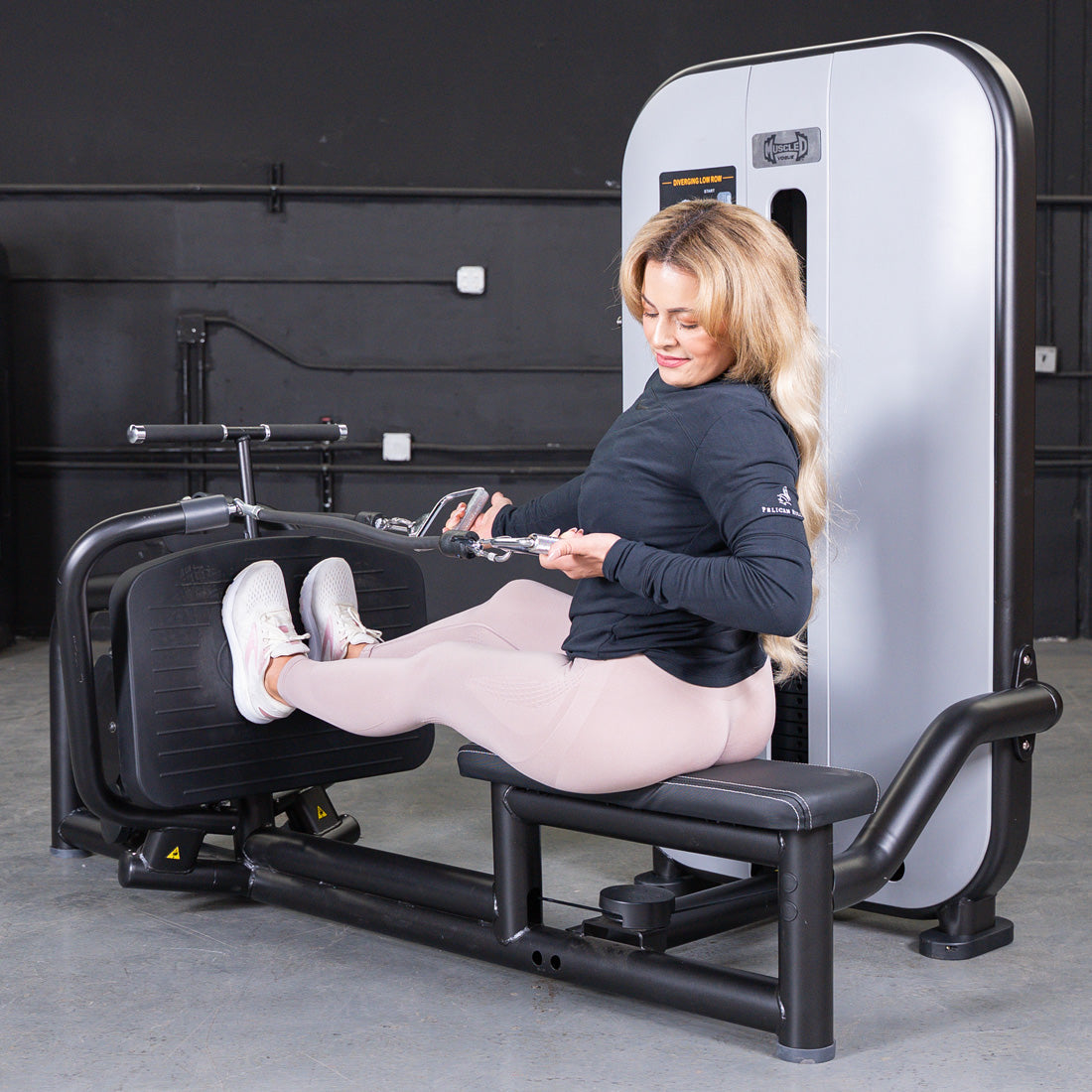 Woman using a low row machine, pulling the handles towards her torso.