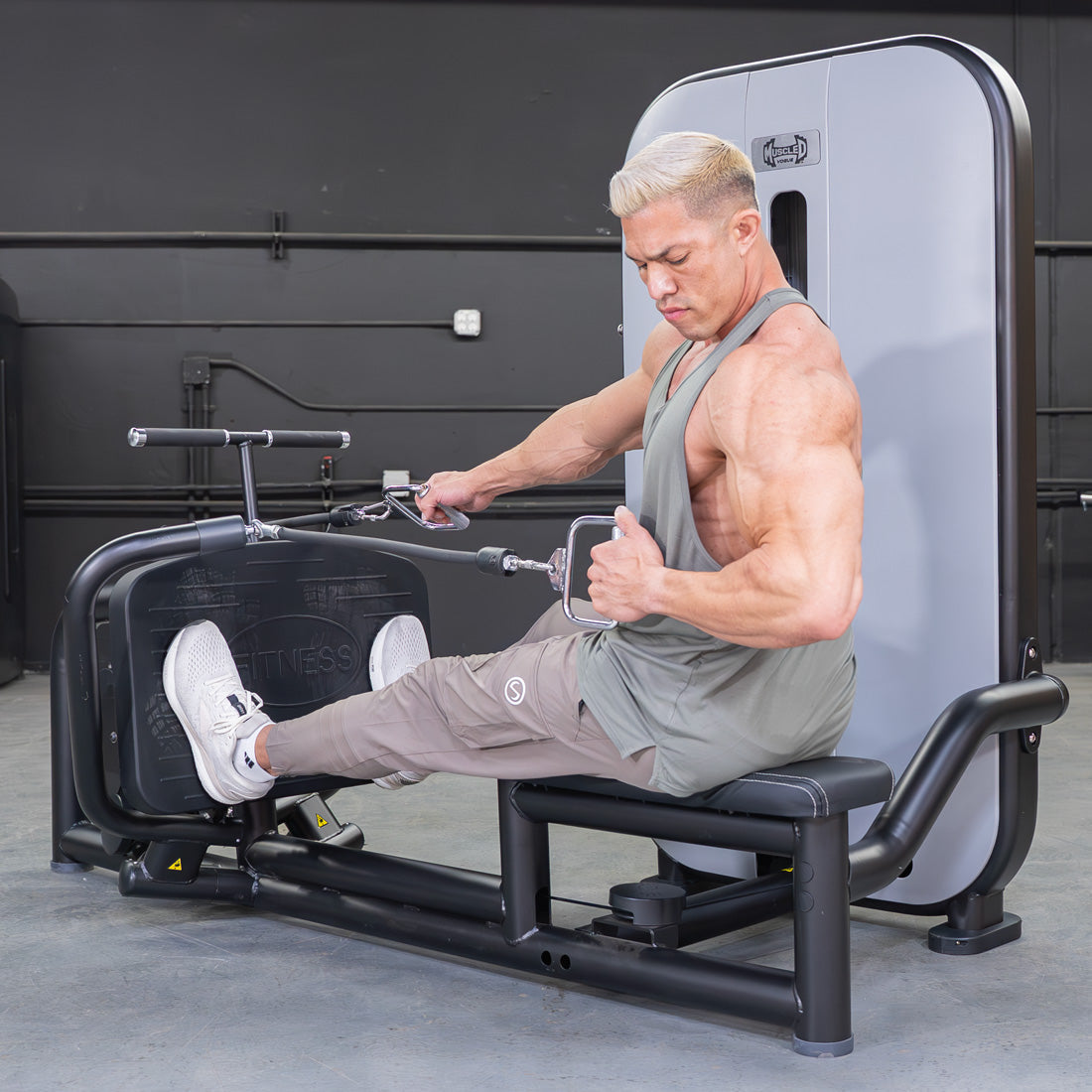 Man in a tank top using a seated low row machine in a gym.