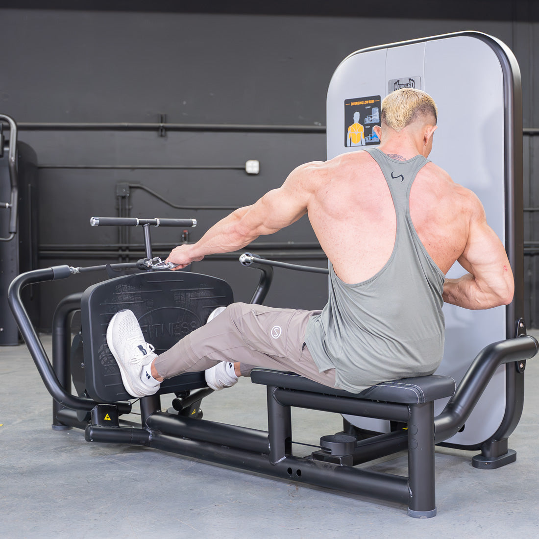 Muscular man in a tank top using a seated low row machine in a gym.