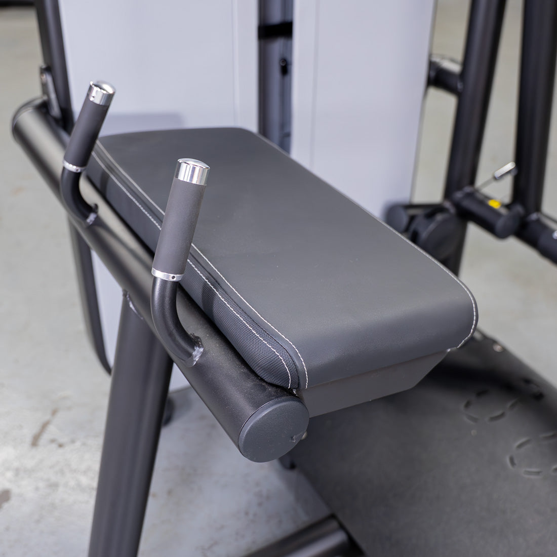 Close-up of a black padded bench with white stitching and two silver-capped handles on a glute extension machine.