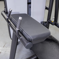 Thumbnail for Close-up of a black padded bench with white stitching and two silver-capped handles on a glute extension machine.