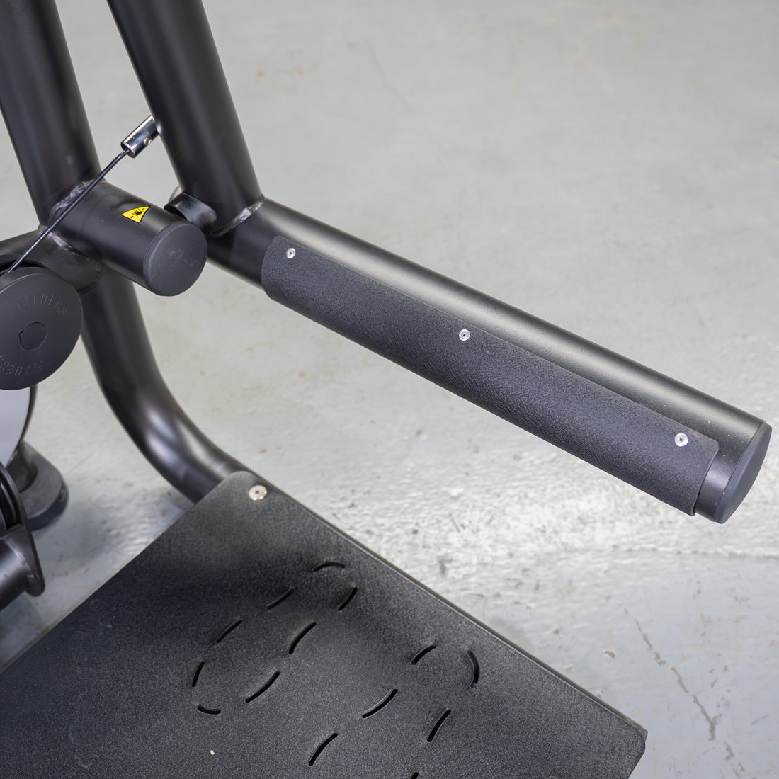 Close-up of the black textured footplate and padded handle of a glute extension machine.