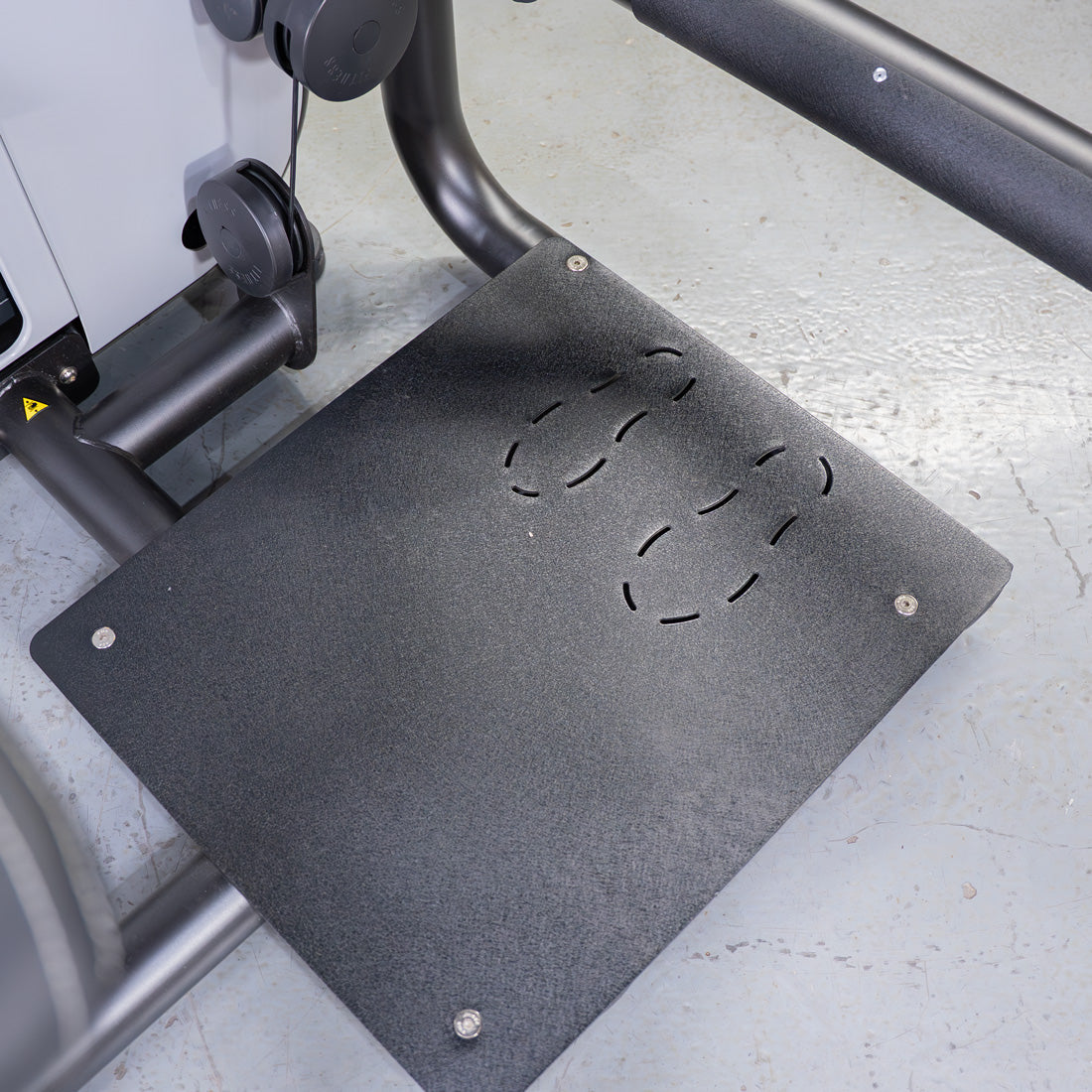 Textured black footplate with four curved cutouts, part of a glute extension machine.