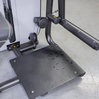 Thumbnail for Close-up of a black glute extension machine with a textured footplate and padded armrest.