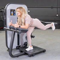 Thumbnail for Woman in pink activewear using a glute extension machine, giving thumbs up.